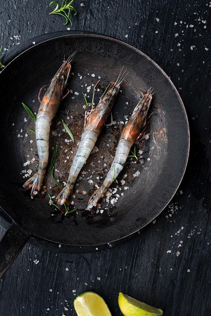 Raw king prawns with salt and herbs in frying pan