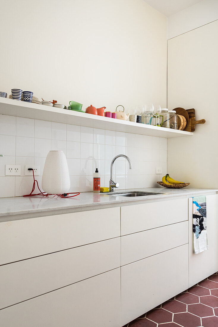 White fitted kitchen, with an open shelf holding colorful dishes