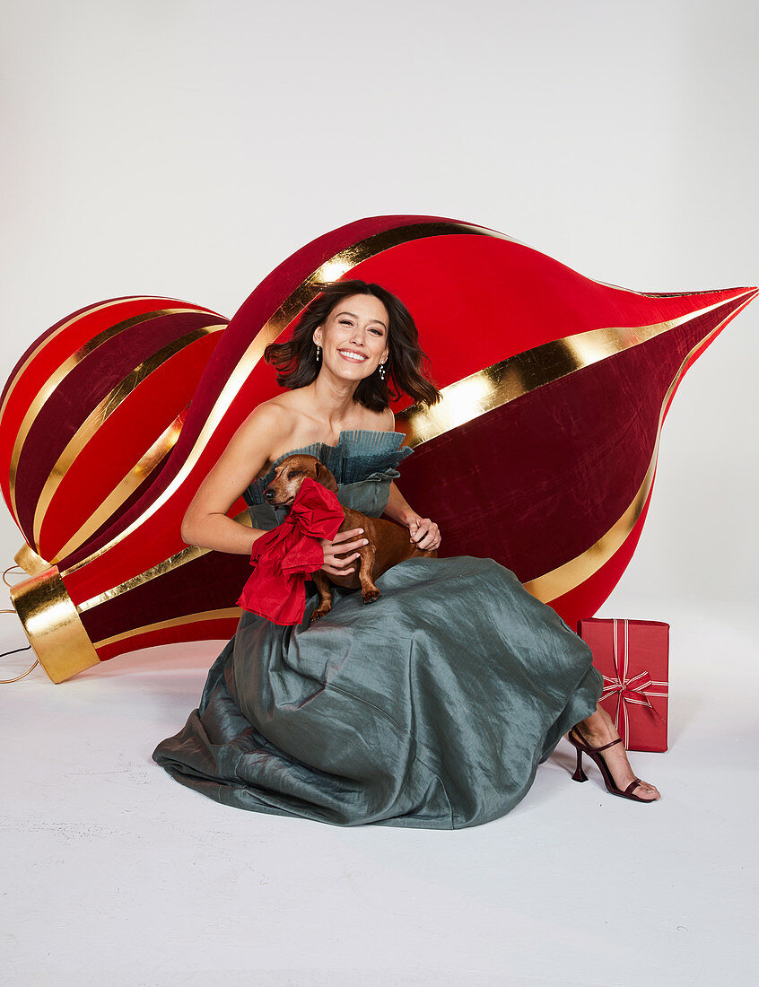 A young woman wearing a festive, strapless dress with a dog and Christmas decorations