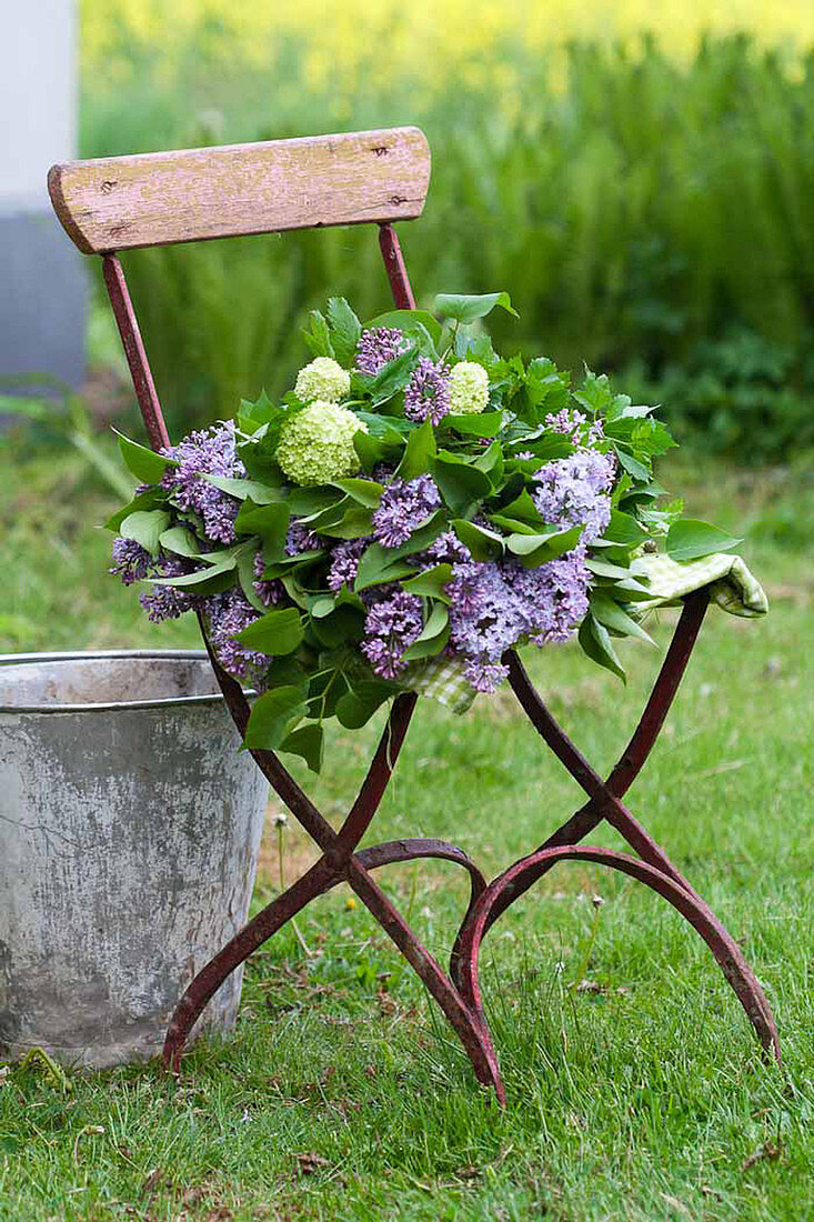 Bouquet of lilac and viburnum on chair in garden