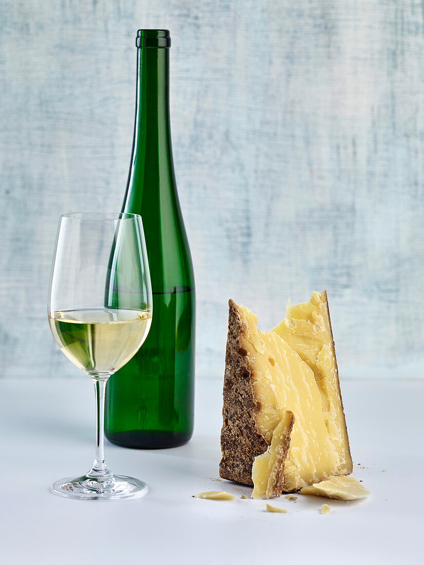 A glass and a bottle of white wine next to a piece of hard cheese