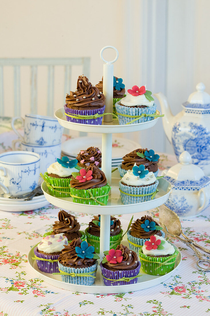 Cupcakes mit bunten Manschetten und Zuckerblumen auf Etagere