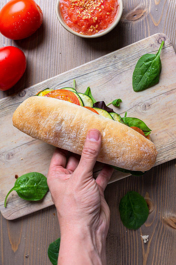 Hand hält ein Panini mit Zucchini und Tomaten