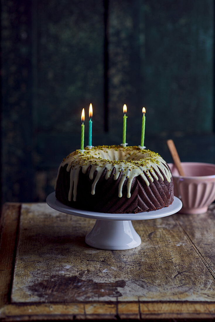 Chocolate Bundt cake with a pistachio glaze and four burning candles