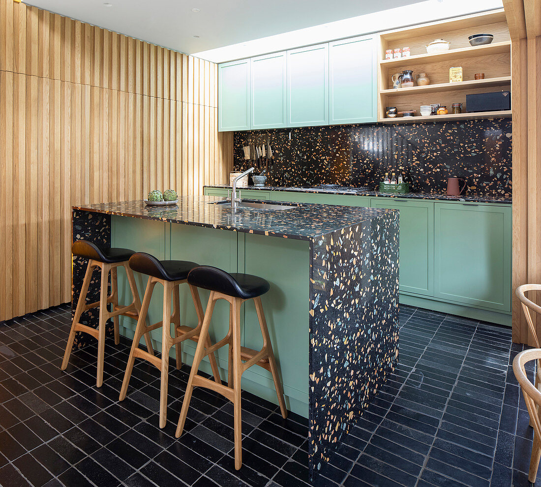 Black terrazzo island counter and green cabinets in open-plan kitchen