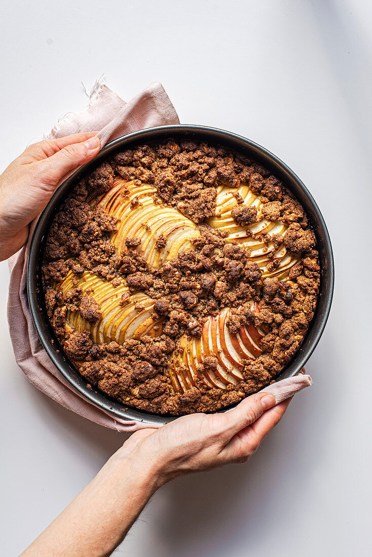 Hände halten Backform mit Apfel-Streusel-Kuchen