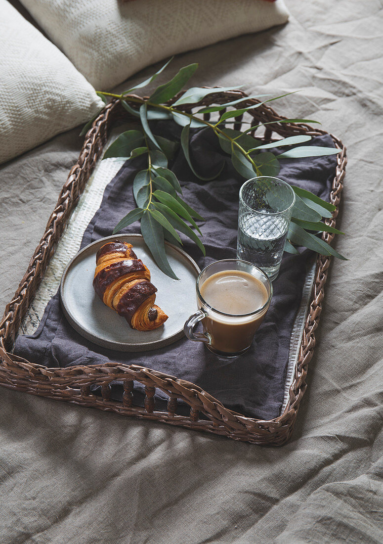 Breakfast in bed - Wicker tray with coffee and croissant on a linen bed