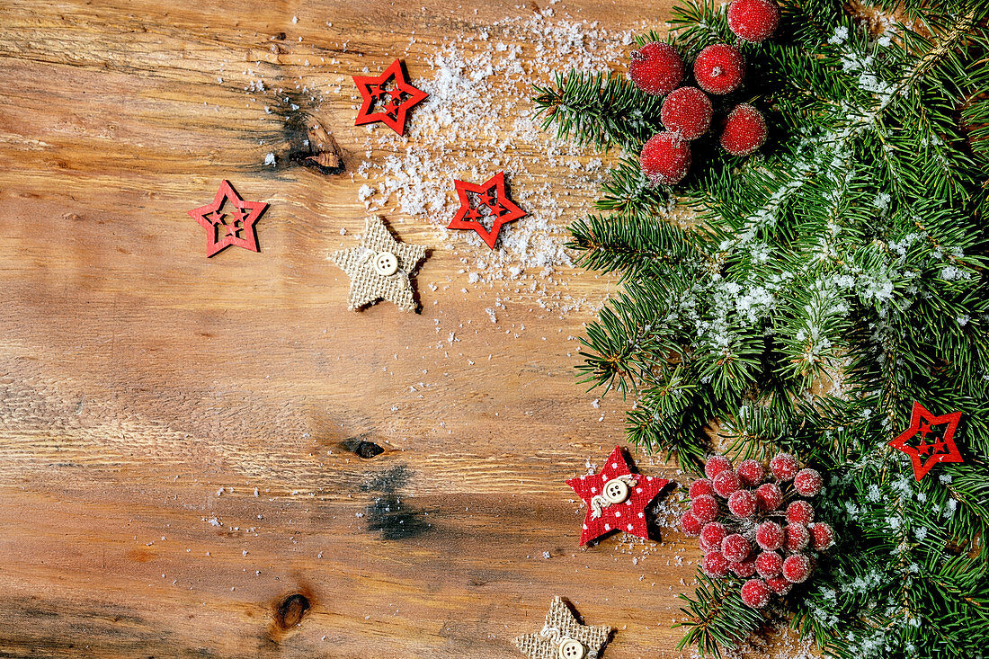 Fir tree branches, red berries and stars over wooden background