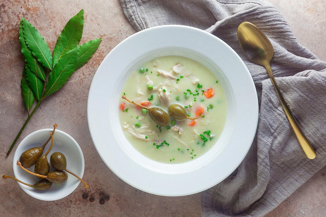 A bowl of chicken fricassee with peas, carrots and caperfruits