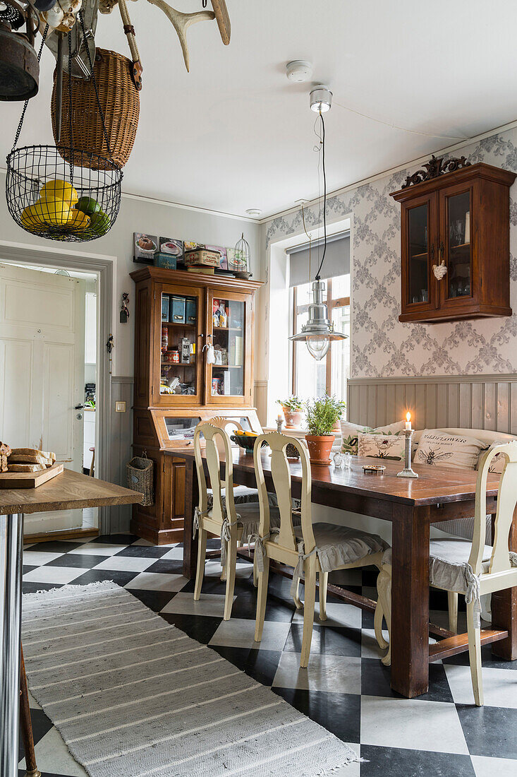 Wooden table with chairs and antique display cabinet in kitchen with chequered floor tiles