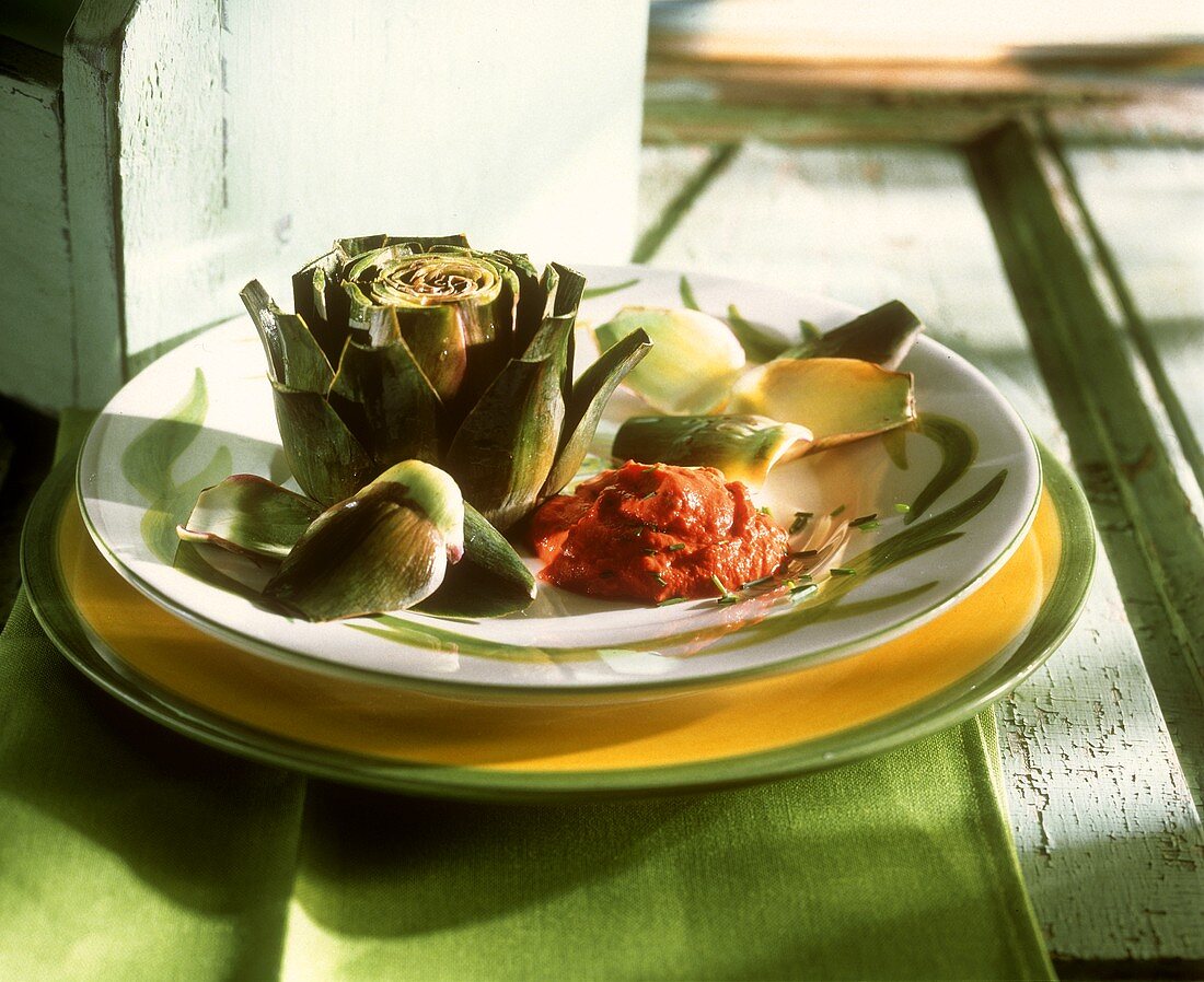 Boiled artichoke with tomato dip on plate