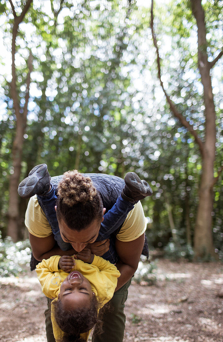 Playful father holding daughter upside down in woods