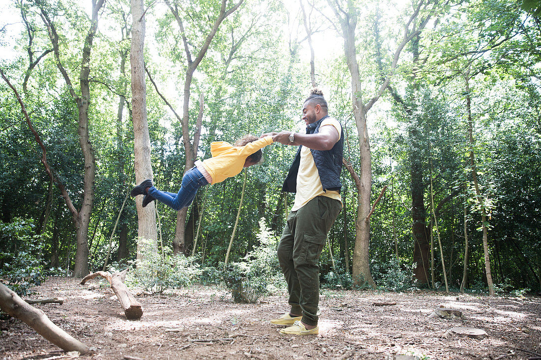 Playful father swinging daughter below trees in woods