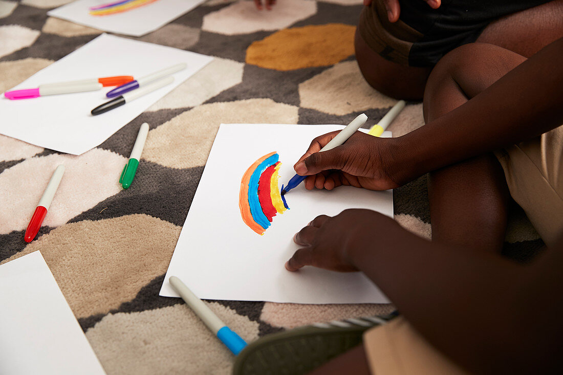 Boy drawing multicolour rainbow with markers on rug