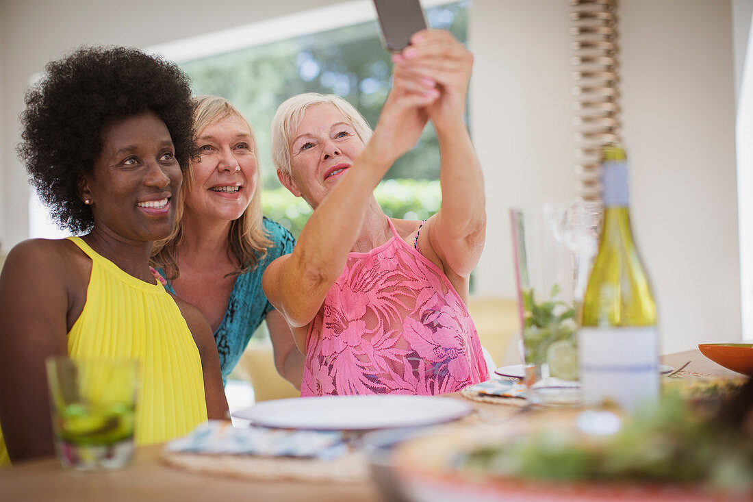 Senior women friends taking selfie at dining table
