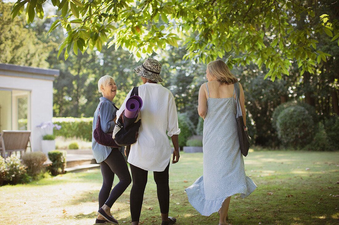 Happy senior women friends with yoga mat in garden