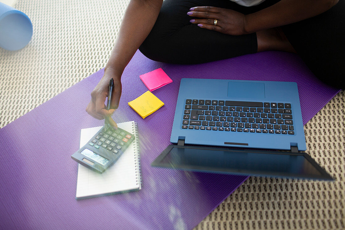 Woman paying bills at laptop on yoga mat at home