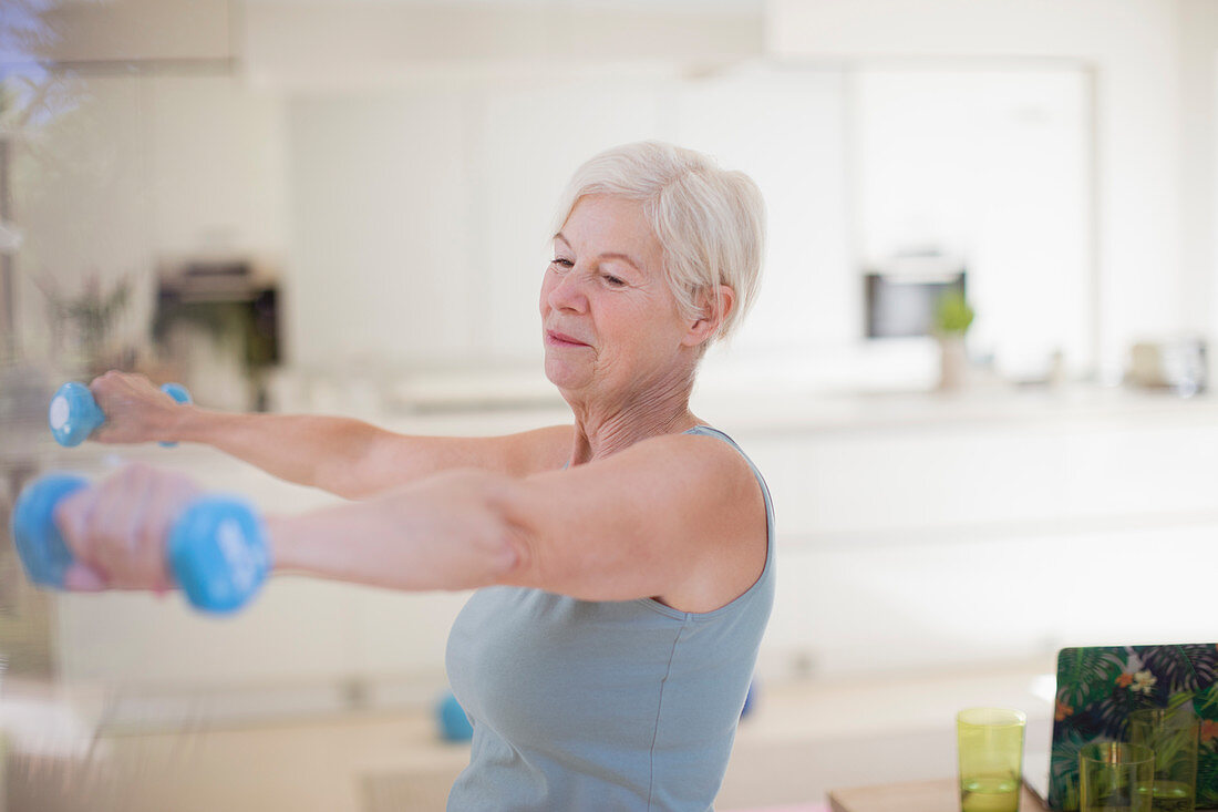 Senior woman exercising with dumbbells in kitchen