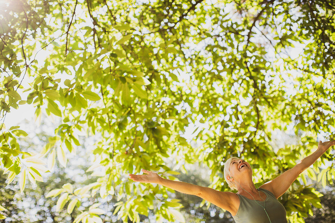 Exuberant senior woman with arms outstretched under tree