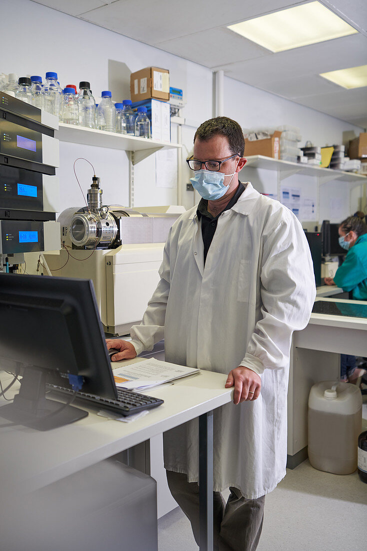 Male scientist in face mask using computer in laboratory