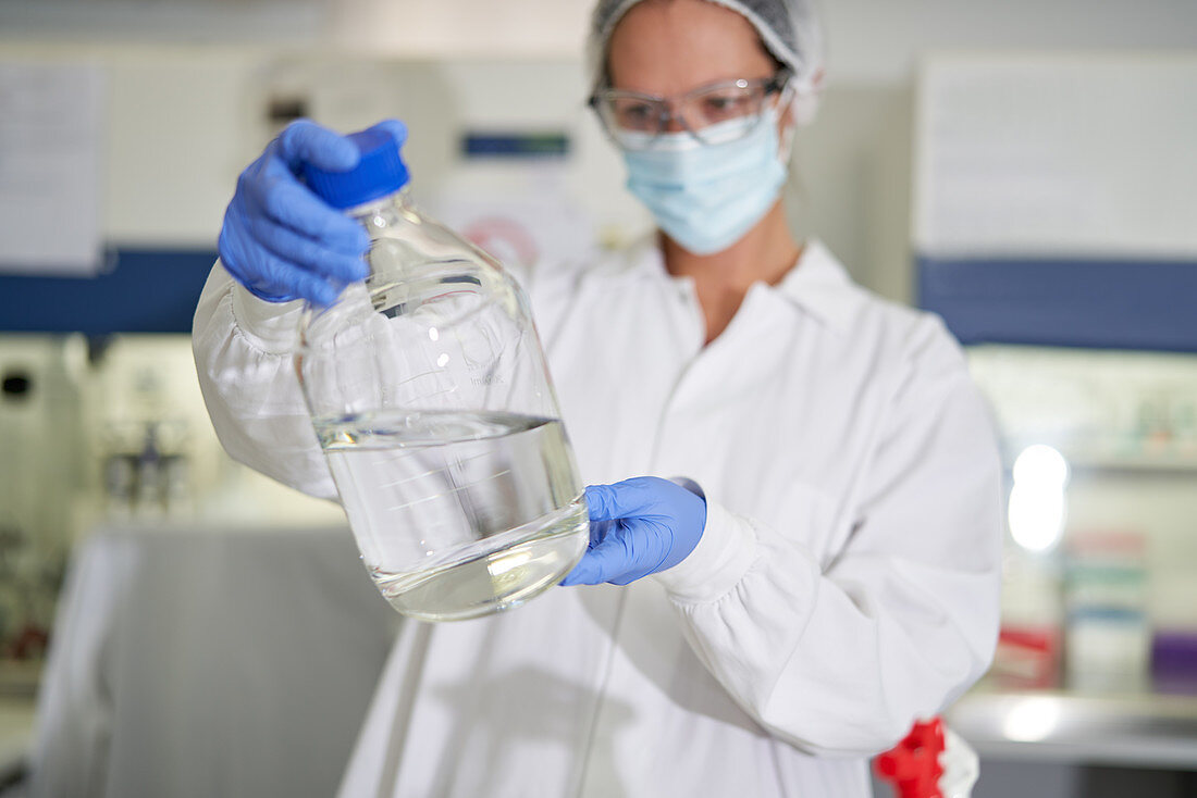 Scientist in face mask and glove examining liquid