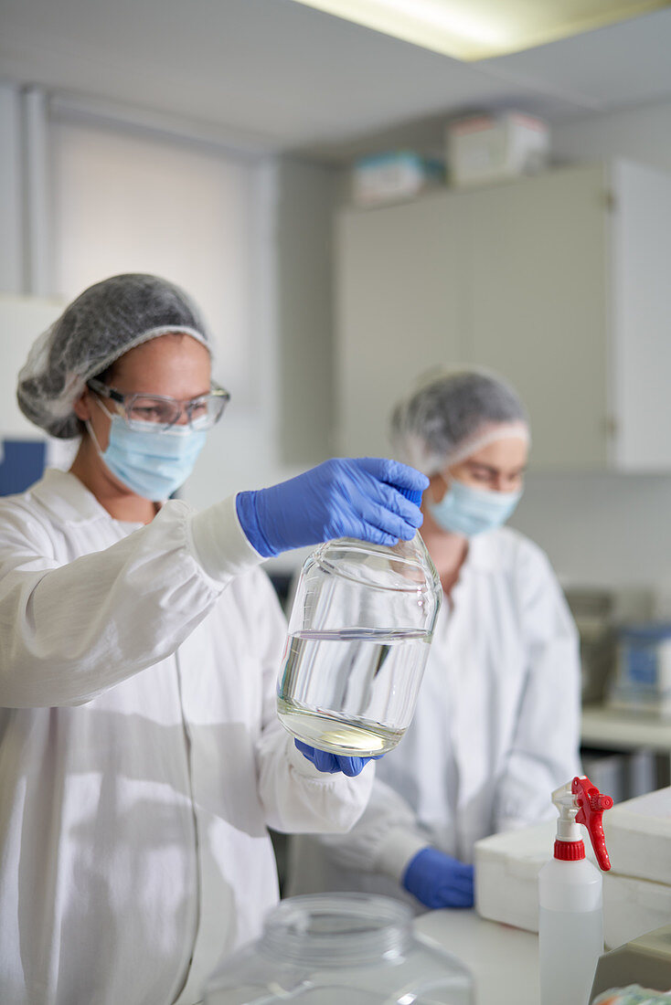 Scientists in protective workwear examining liquid