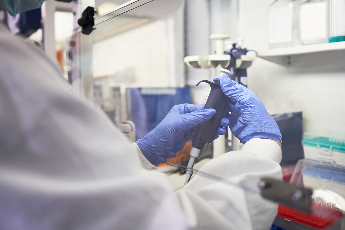 Scientist using pipette under fume hood in laboratory
