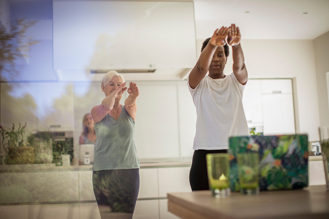 Senior women friends exercising at laptop in dining room