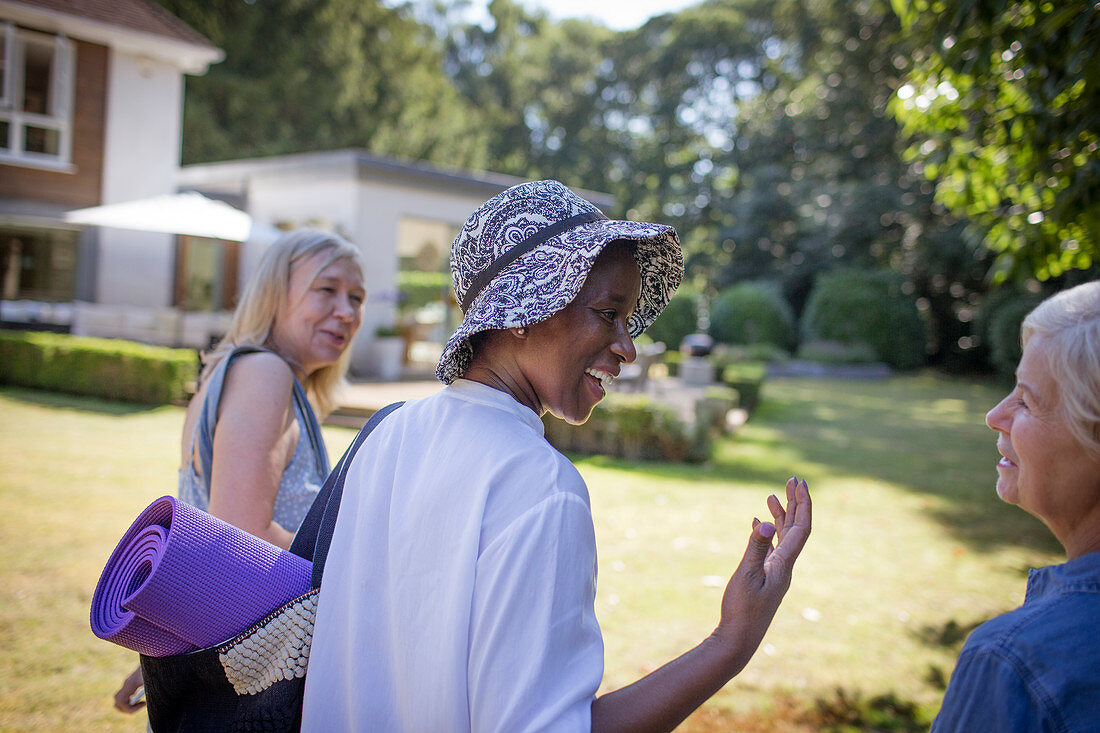 Happy senior women friends with yoga mat in garden