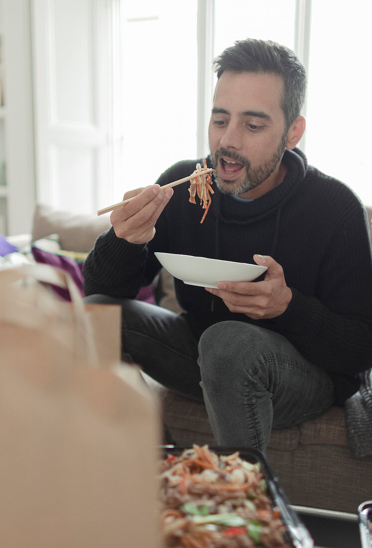 Man eating takeout noodles with chopsticks