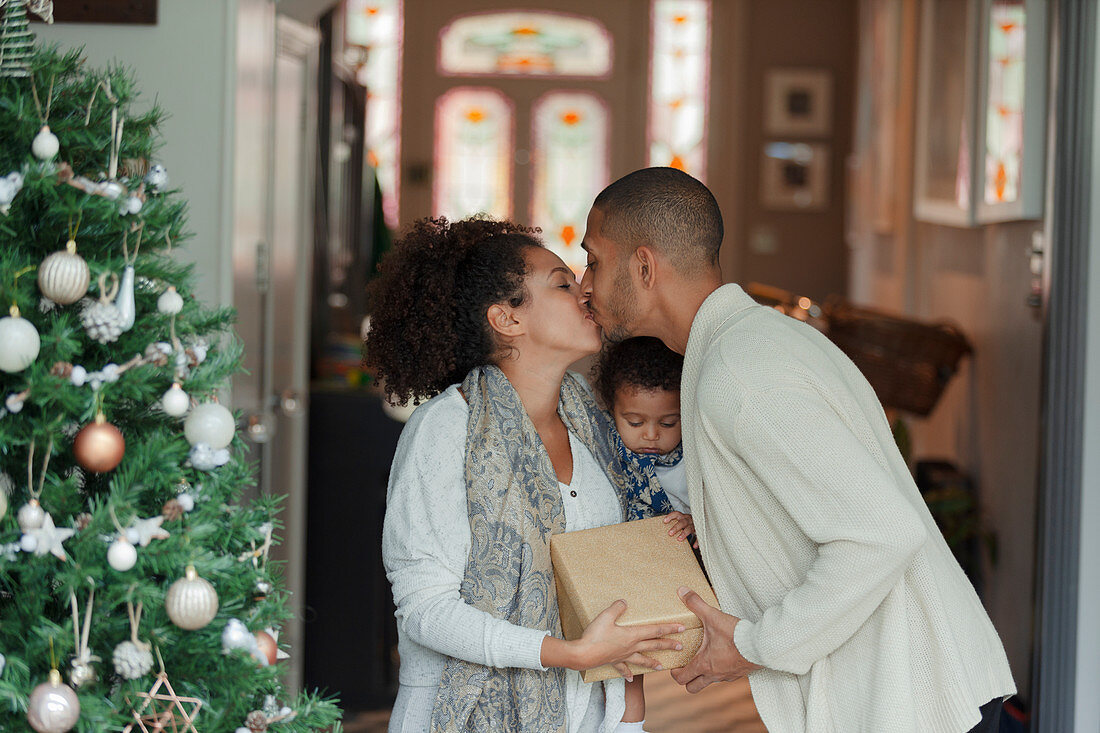 Couple with baby daughter kissing at Christmas tree