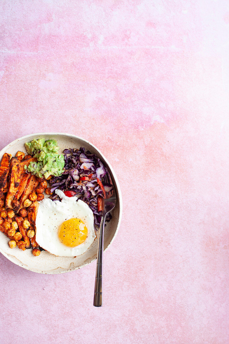 Buddha bowl with fried egg, oven baked sweet potato, spicy chickpeas, red cabbage salad and guacamole