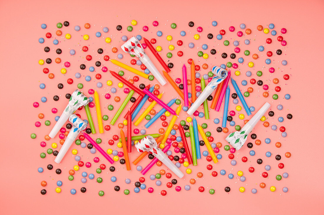 Colorful sprinkles, blowers and birthday candles on pink background
