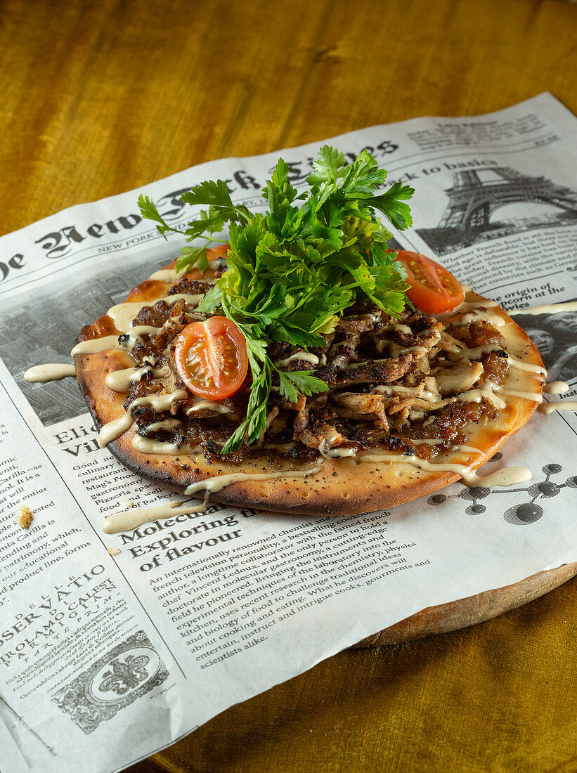 Chicken shawarma on a grilled pita, tomatoes, tahini and parsley