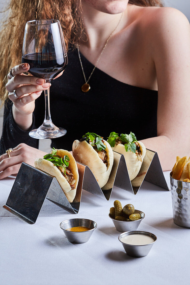 A model in a restaurant with red wine and chicken shawarma in pita, pickles, Amba, tahini and french fries