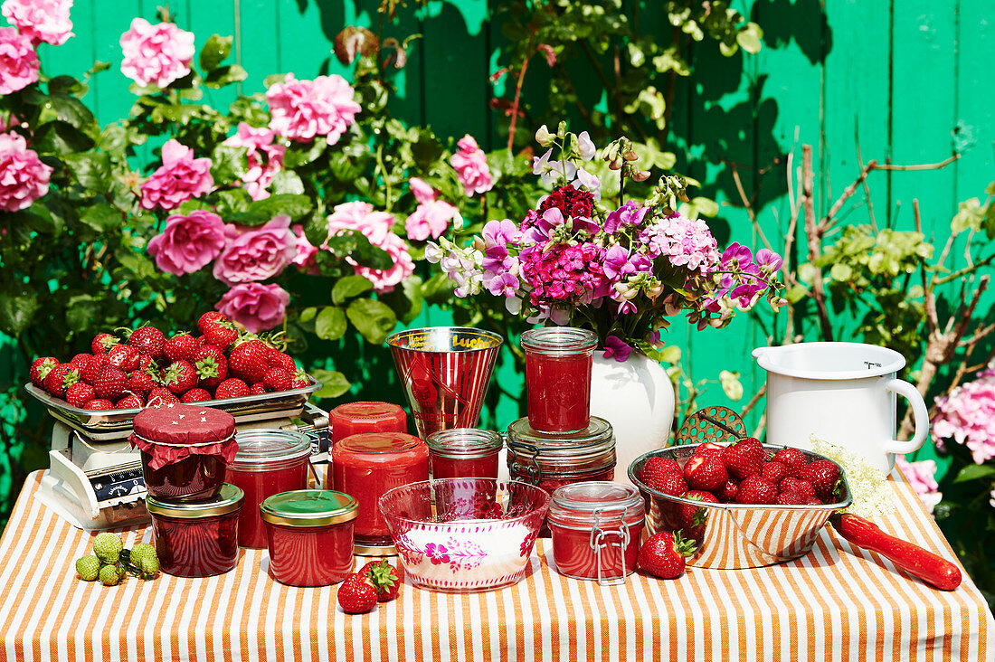 Selbstgemachte Erdbeermarmelade in Gläsern auf Tisch im Garten