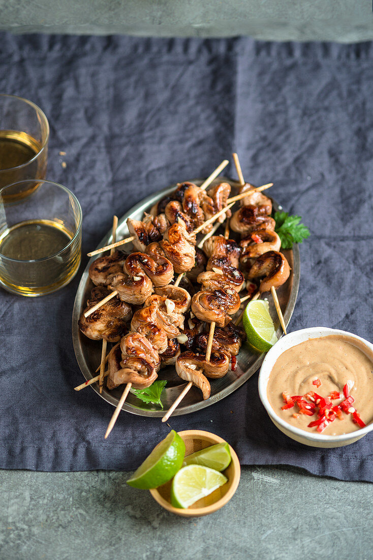 Thai chicken satay skewers on a silver tray served with peanut sauce and fresh lime