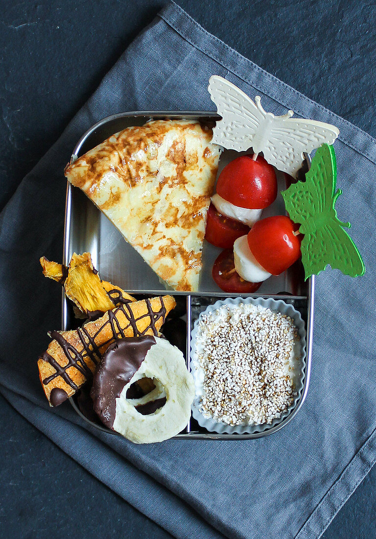 A breakfast box with tortillas, tomatoes on sticks, yoghurt and fruit chips