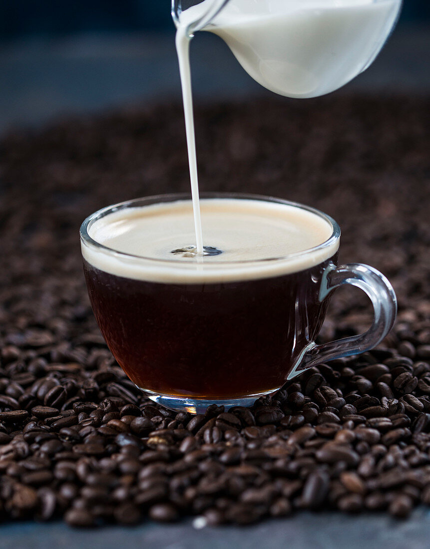 Milch wird in Tasse Kaffee gegossen