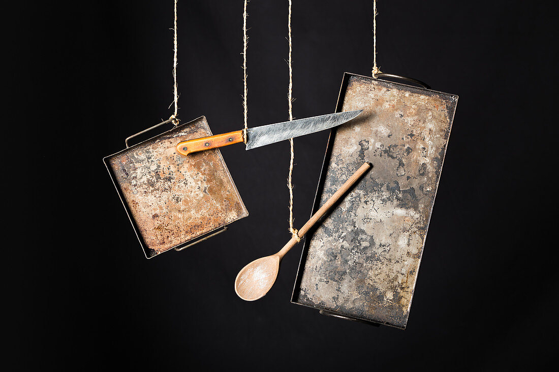Rustic metal baking sheets, knife and wooden spoon hanging on ropes