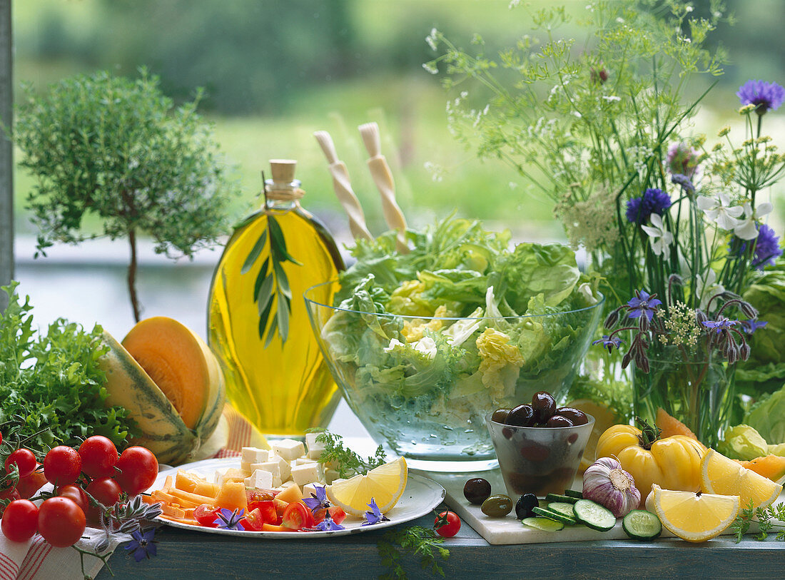 Sommerliches Stillleben mit Kopfsalat, Oliven, Feta, Melone, Tomaten, Olivenöl, Kräutern