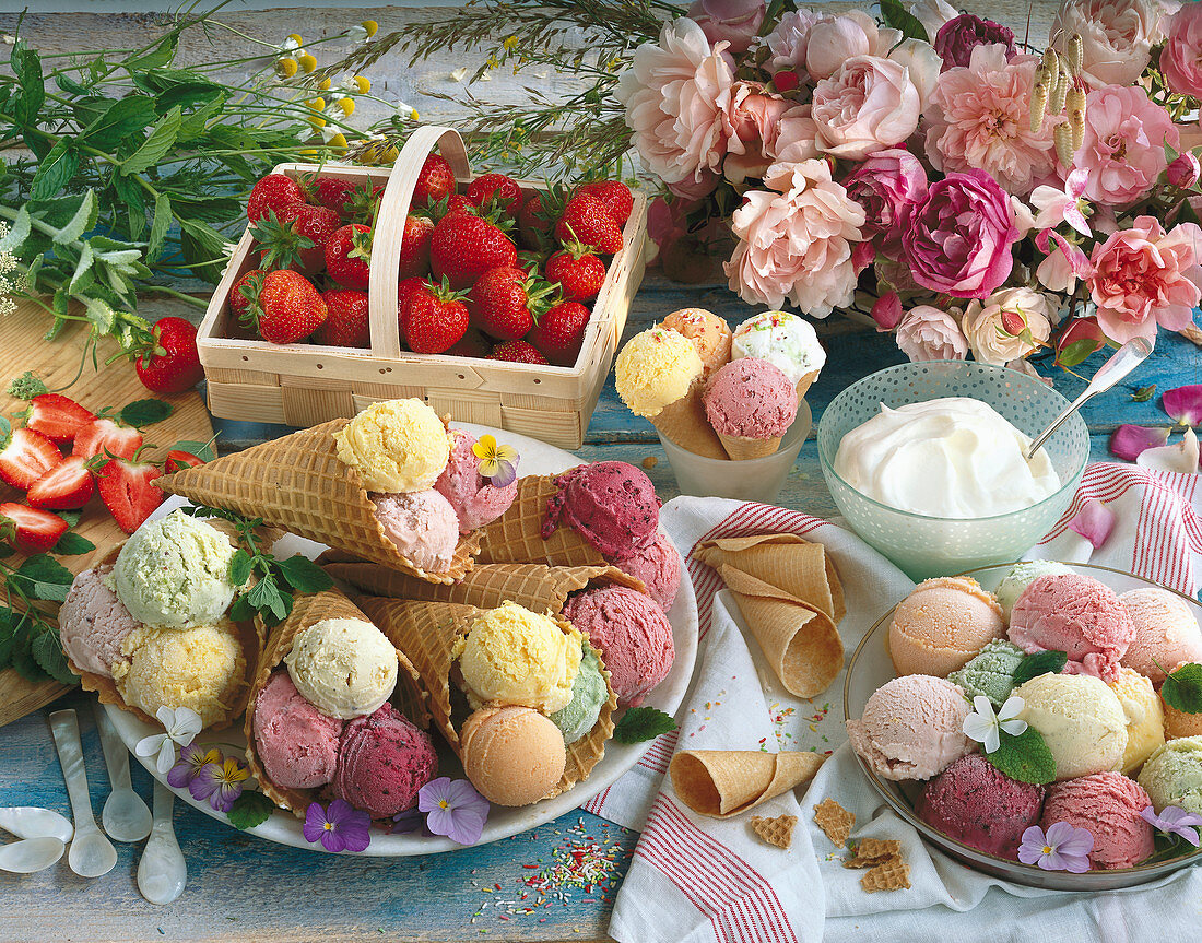 Stillleben mit mehreren Eistüten, Eiskugeln, Erdbeeren und Schlagsahne