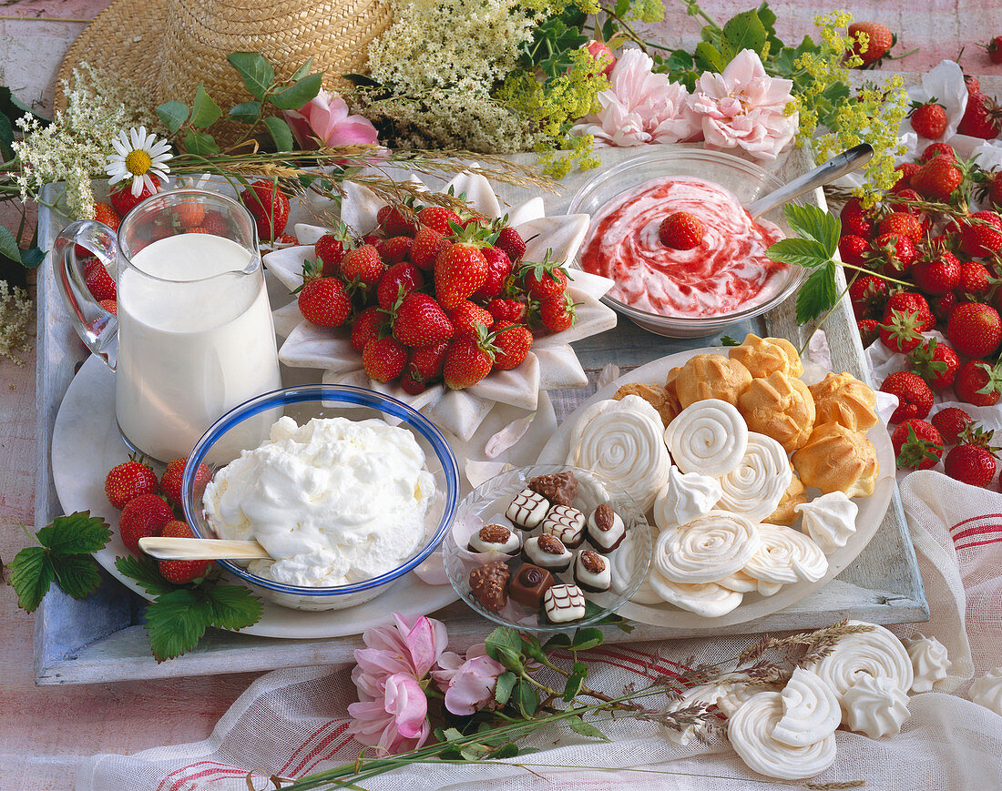 Stillleben mit Erdbeeren, Erdbeerquark, Windbeuteln Baiser, Pralinen, Schlagsahne und Milch