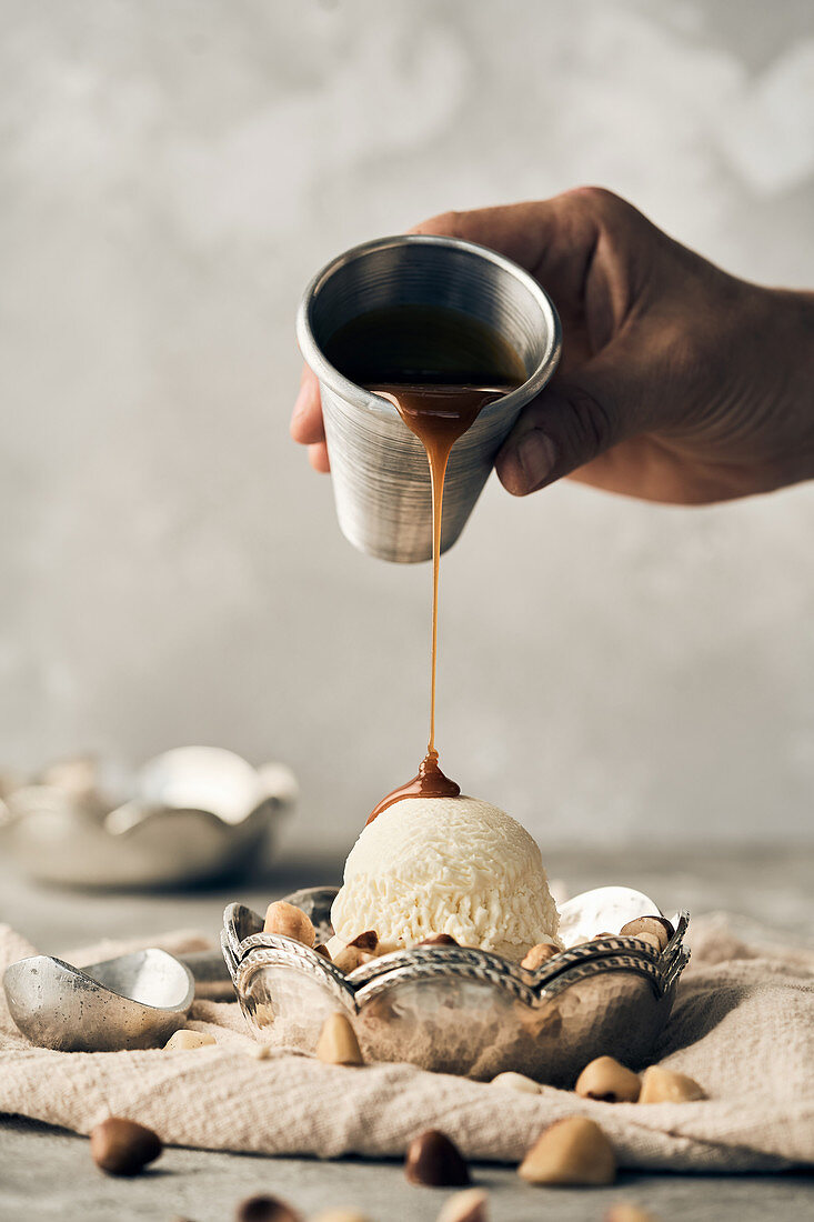 Pouring sweet caramel topping on vanilla ice cream scoop