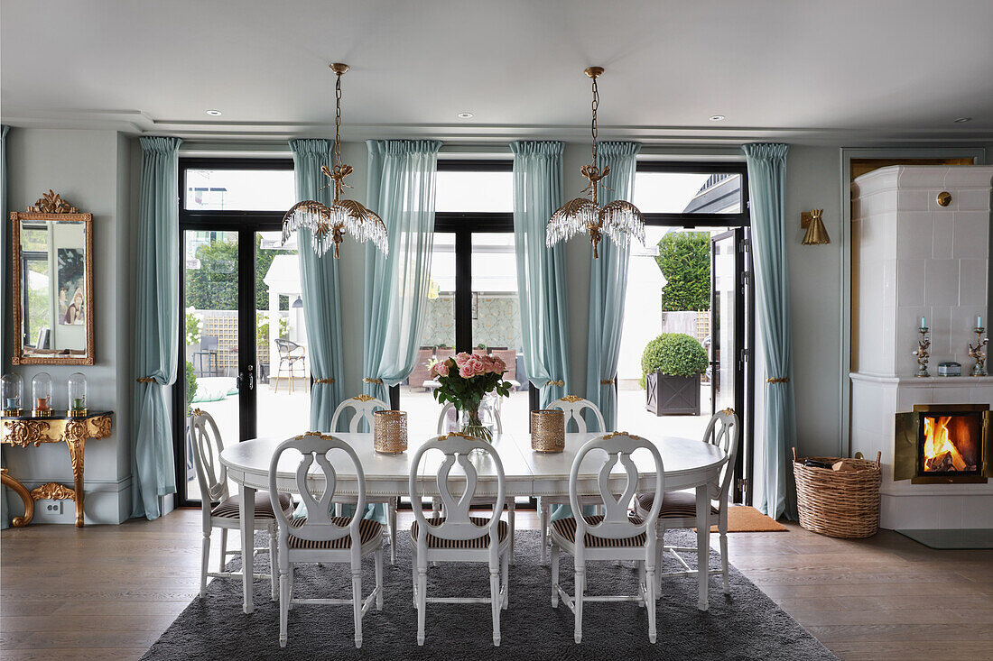 White dining table with chairs in open living room with French doors and blue curtains