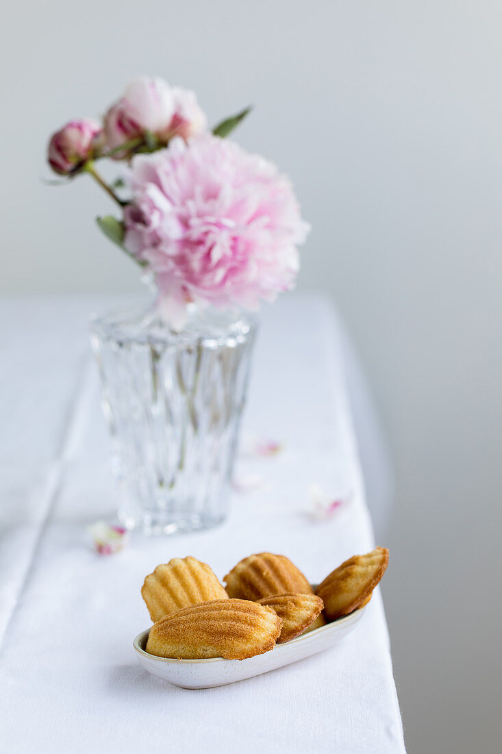 Madeleines in a small bowl in front of a vase with peonies