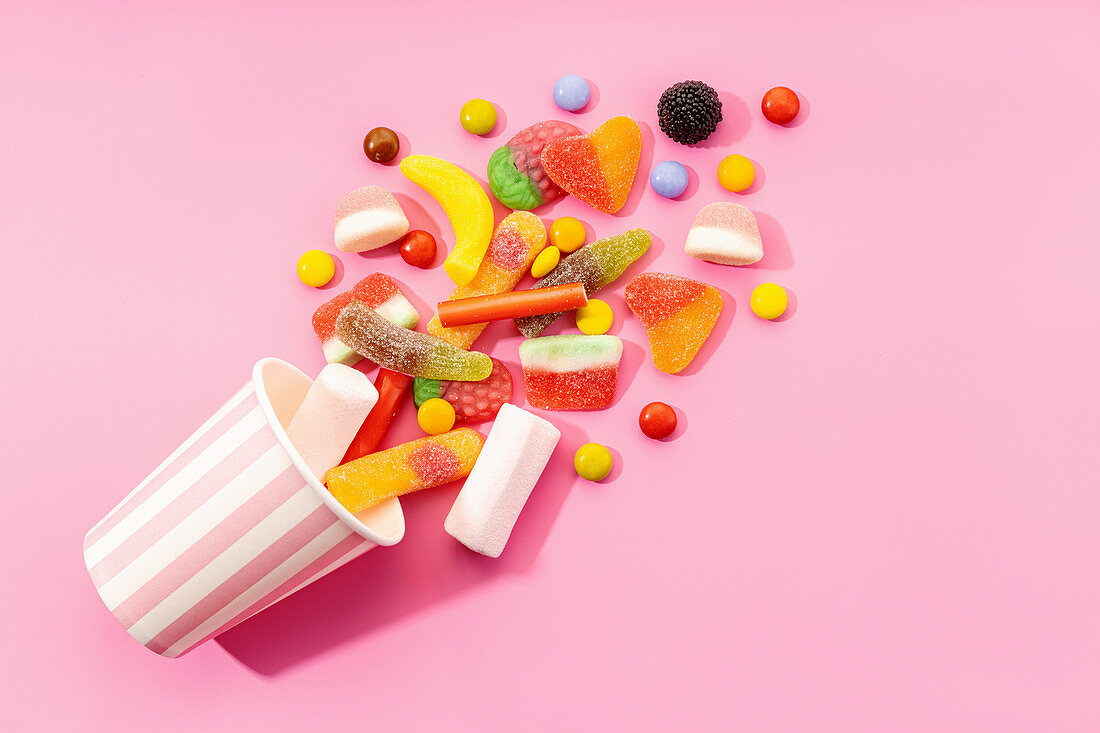 Multicolored jelly candies and marshmallows scattered on pink background