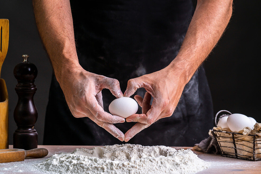 hands building heart shape while holding raw chicken egg over flour