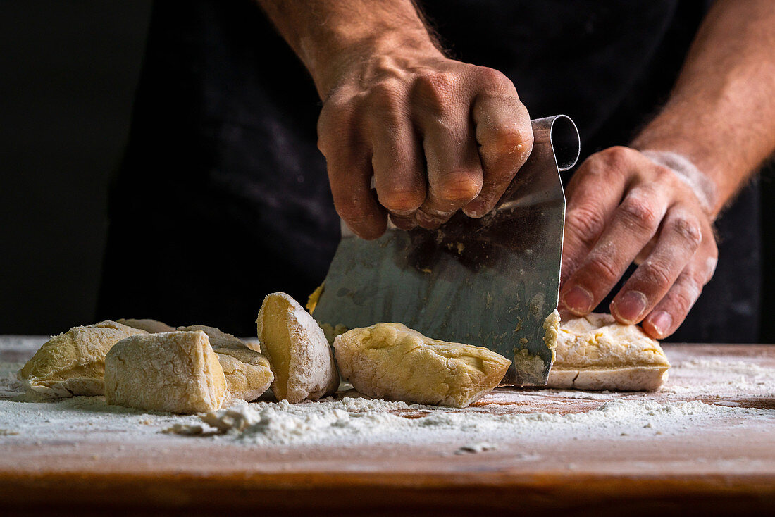 Man dividing raw bread dough with scraper