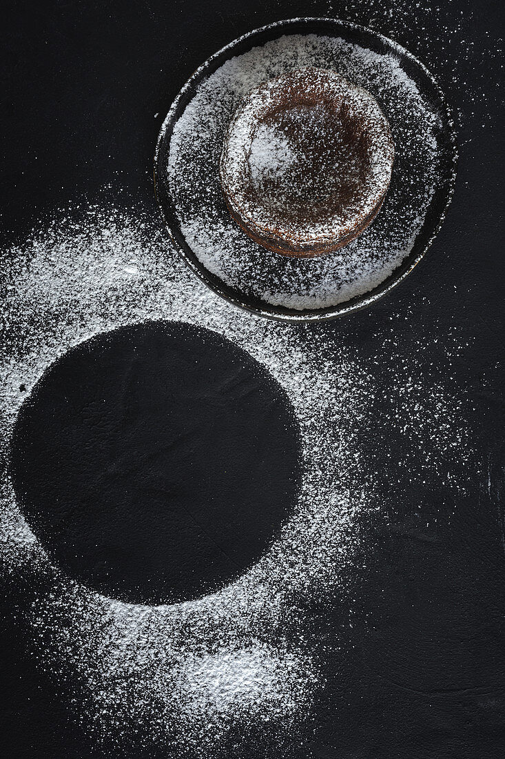 Chocolate coulant on black background with sugar powder circle